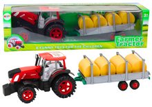 Velký zemědělský traktor s přívěsem a balíky sena červený
